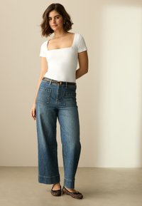 Body blanc à manches courtes avec un décolleté carré, associé à un jean denim bleu à jambes larges avec poches arrière et ourlet retroussé. Chaussures plates imprimé léopard.