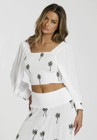 Top corto blanco y falda a juego, ambos con una tela texturizada; adornados con bordados de palmeras en negro y dorado. Escote cuadrado, mangas abullonadas.