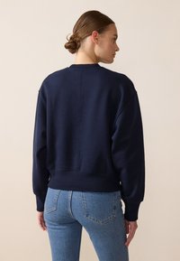Felpa blu navy con una vestibilità comoda, polsini e orlo a costine, morbida al tatto e con dettagli di cucitura minimi, abbinata a jeans azzurri.