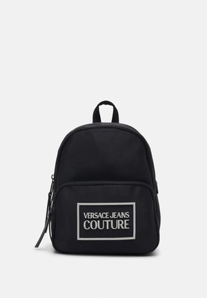 Mochila negra con bolsillo frontal con cremallera y logotipo blanco de Versace Jeans Couture centrado en el bolsillo sobre un fondo liso.