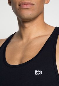 Svart tanktopp laget av myk bomull, med rund hals og en liten hvit brodert "Lee"-logo på brystet.