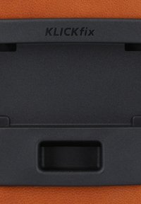 Supporto KLICKfix in plastica nera opaca, con un design rettangolare dotato di una fessura orizzontale e un'area incavata su uno sfondo arancione testurizzato.