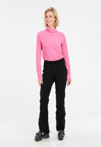 Ilgo rankovės, raukšlėtas turtlenekas ryškiai rausvos spalvos, derinamas su prigludusiais juodais slidinėjimo kelnais ir juodais slidinėjimo batais, demonstruojantis stilingą, modernų siluetą.