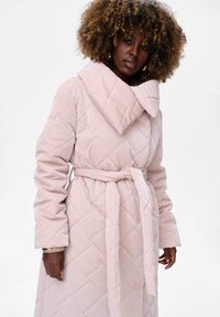 Gevoerde, gewatteerde kimono in lichtroze met een brede kraag, lange mouwen en een strikceintuur in de taille. Heeft een gladde, glanzende textuur.