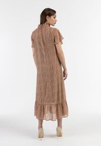 Brun blomsterkjole med korte ærmer, bølget halsudskæring og lagdelt kant, lavet af letvægtsstof med en blød tekstur. Beige højhælede sko.