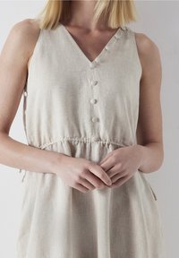 Robe beige clair en lin, avec un col en V, des boutons décoratifs et une taille élastique pour une coupe décontractée.