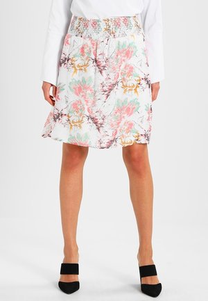 Jupe florale avec une taille smockée, ornée de motifs roses, verts et jaunes sur fond blanc, associée à des chaussures à talons noires.