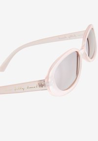 Rózsaszín áttetsző macskaszem napszemüveg színezett lencsékkel és arany színű kézírásos felirattal az egyik szárán, fehér háttér előtt.