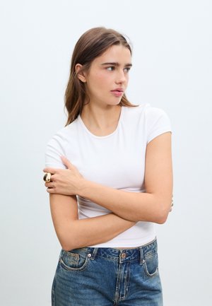 Vit t-shirt med korta ärmar, slät textur, kombinerad med jeans i hög midja av denim med klassiska fickor och en ljusblå tvätt.