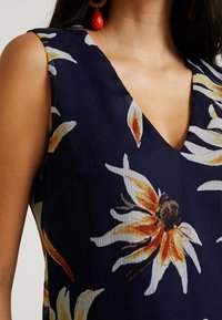 Abito senza maniche di colore navy con scollatura a V, caratterizzato da un motivo floreale giallo e bianco, realizzato in un tessuto testurizzato con un leggero lucido.