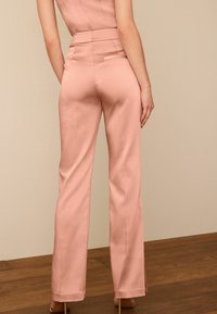 Pantalon en tissu rose clair, design à jambes larges sur mesure, texture douce, avec une taille ajustée et des poches latérales.
