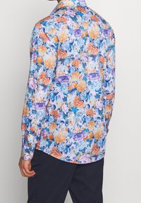 Camisa de manga larga con estampado floral que presenta un fondo azul claro con flores multicolores, incluyendo acentos naranjas, morados y azules.