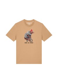 Beige T-Shirt mit einem Bären in einem gestreiften Outfit und einer roten Mütze, der auf einem Einrad fährt, mit dem Text "GEBOREN UM FREI ZU SEIN" unter dem Motiv.