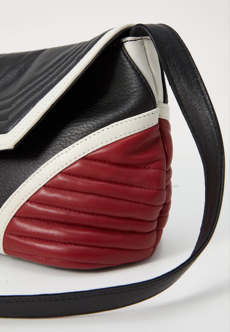 Gepolsterte Handtasche aus schwarzem und rotem Leder mit einem weißen Rand. Das Design ist eckig und strukturiert und verfügt über einen einzelnen Tragegurt.