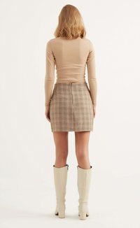 Beige geripptes Langarmoberteil, kombiniert mit einem karierten Minirock mit strukturierter Oberfläche und einem Reißverschluss hinten, ergänzt durch kniehohe cremefarbene Stiefel.