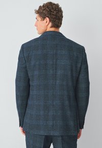 Marinblå rutig kavaj i en texturerad tygkvalitet, med en skräddarsydd passform, snibbade laplar och knäppte manschetter. Synliga sömdetaljer på baksidan.