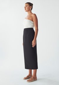 Jupe midi noire avec une coupe ajustée, dotée d'une taille haute et de détails plissés, associée à un haut sans manches blanc à côtes et des sandales minimalistes.