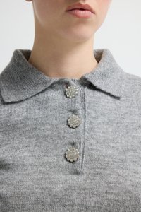 Grijze gebreide trui met een kraag en drie decoratieve, glinsterende knopen bij de hals. Gladde textuur met subtiele glans.
