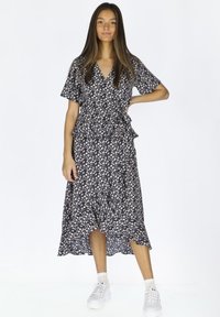 Florales Wickelkleid in Marineblau mit kurzen Ärmeln, Rüschensaum und weißem Blumenmuster. Kombiniert mit weißen Sneakers. Leichter Stoff.