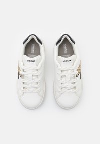 Baskets blanches en cuir texturé, avec des accents noirs et un détail décoratif doré. Elles disposent d'un système de laçage et d'un intérieur en maille respirante.