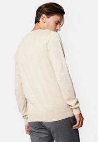 Jasno beżowy sweter z dzianiny z okrągłym dekoltem, ściągaczami na mankietach i u dołu. Charakteryzuje się gładką fakturą i dopasowanym krojem.