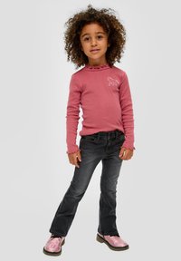 Roze longsleeve top met ruches aan de mouwen en een paardenafbeelding, gecombineerd met zwarte jeans en glanzende roze laarzen.