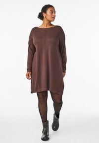 Bruine gebreide jurk met lange mouwen en een ronde hals, met een losse pasvorm en een rechte zoom, gedragen met zwarte enkellaarzen.