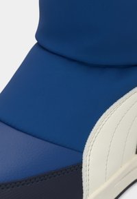 Baskets en textile bleu avec une finition lisse, un design superposé avec des accents blancs et des coutures détaillées le long des contours.