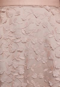 Tissu avec des appliques florales roses translucides et des feuilles brodées sur un fond en maille rose clair, montrant des motifs délicats de fleurs et de feuilles.