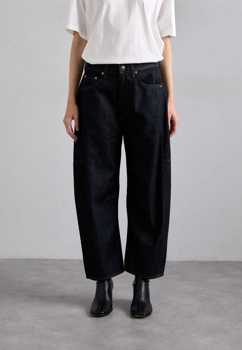 Dark denim wide-leg trousers with front pockets, top button closure, and visible stitching details. Worn with a white t-shirt and black boots.