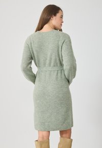 Rochie tricotată de culoare verde, cu talie marcată printr-un brâu, mâneci lungi și textură striată, care se termină chiar deasupra genunchiului. Material moale și confortabil.