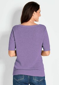 Lila gestrickter Pullover mit kurzen Ärmeln, Boot-Ausschnitt und Rippenbund. Weiche Textur, lässige Passform, kombiniert mit blauen Jeans.