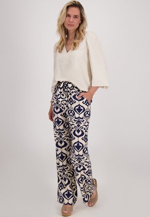 Lichtbeige blouse met een V-hals en pofmouwen, gecombineerd met wijde broek met een marineblauw en crèmekleurig bloemenpatroon.