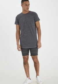 Gray short-sleeve t-shirt with a round neck, paired with dark plaid shorts and white sneakers. The fabric appears soft and casual.