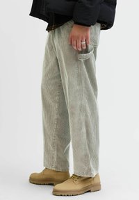 Lysegrønne cordfløyelbukser med rette ben, som har vertikale striper og en sidelomme, kombinert med brune snøreboots.