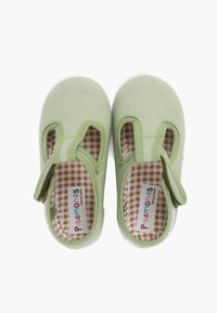 Zapatillas de lona verdes con lados cortados y tira de Velcro, con una plantilla de cuadros marrones y blancos. Suela de goma blanca.