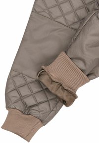 Brunt quiltet stof med en glat finish. Flæsekantede, ribstrikkede manchetter i en matchende nuance. Har et geometrisk mønster for ekstra tekstur.