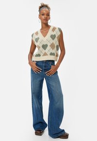 V-hals ærmeløs strikket sweater med et beige, grønt og brunt argyle mønster. Sammen med vide blå denim jeans. Brune platform sko.