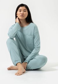 Ensemble lounge bleu clair en tissu doux ; haut à manches longues avec col rond et poche, pantalon tapered avec poignets élastiques, chevilles découvertes.