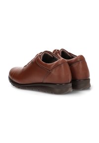 Zapatos de cuero marrón con punta redondeada, textura suave y suela de goma baja. Presentan costuras mínimas y un detalle de logo sutil en el lateral.