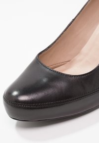 Gros plan sur la partie avant d'une chaussure pour femme en cuir noir, avec un bout arrondi et un détail de semelle cousue, sur fond blanc.