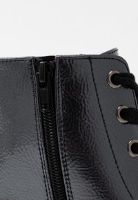 Czarny syntetyczny botek za kostkę o błyszczącej powierzchni, z centralnym zamkiem błyskawicznym i okrągłymi oczkami do sznurowania. Teksturowany materiał na powierzchni.