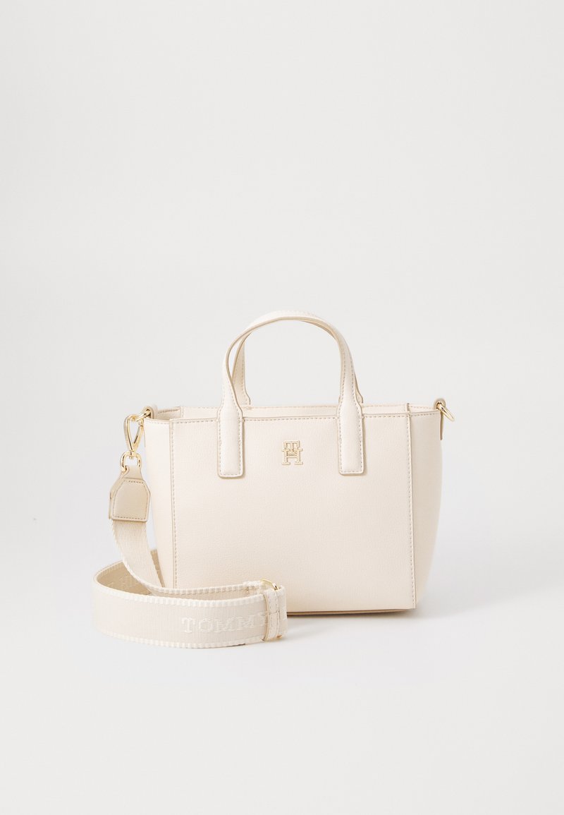 Borsa sintetica beige con due manici corti, hardware dorato e una tracolla removibile con la scritta "TOMMY" in motivo tessuto. Texture liscia.