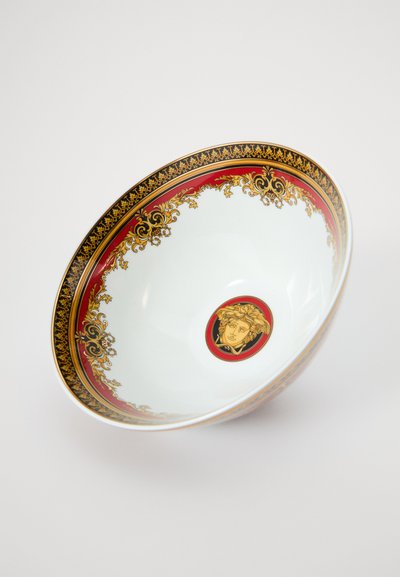 Κεραμικό μπολ με λευκό εσωτερικό και περίτεχνο κόκκινο και χρυσό περίγραμμα· το κεντρικό σχέδιο περιλαμβάνει ένα στυλιζαρισμένο πρόσωπο περιβαλλόμενο από περίπλοκα μοτίβα.