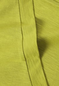 Gros plan d'un tissu vert citron avec une texture de tissage visible et une couture pliée courant verticalement au centre.