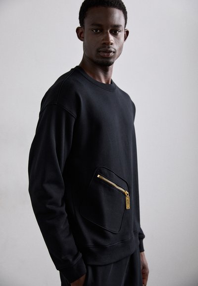 Čierny mikina vyrobená z hladkej tkaniny, s veľkým zipsovým vreckom na prednej strane, so zlatými kovovými doplnkami a zaobleným výstrihom.