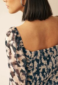 Bloemenprint jurk met een vierkante halslijn, pofmouwen en gerimpeld stof in tinten van crème, marineblauw en grijs. Zachte textuur.