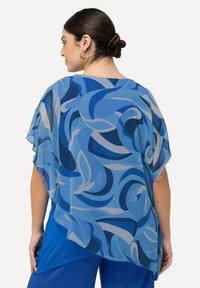 Kimono leggero in chiffon nelle tonalità del blu, presenta swirl astratti e una vestibilità ampia. Le maniche affusolate e l'orlo curvo accentuano il suo design fluttuante.