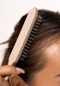 Spazzola per capelli con un manico beige, dotata di setole nere e spesse. Viene utilizzata su capelli scuri e lisci vicino al cuoio capelluto.