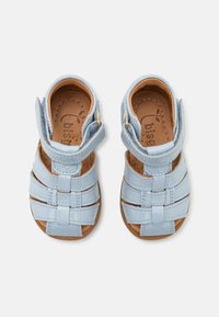 Light blue leather sandals with a woven design, ankle strap, and gold hardware. Smooth texture and brown insoles with logo detail.
